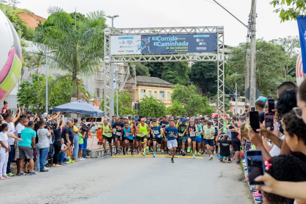 Corredores na largada da Corrida de São Sebastião, realizada em março de 2025, acima do pórtico. Ao lado, dezenas de pessoas acompanham a largada.