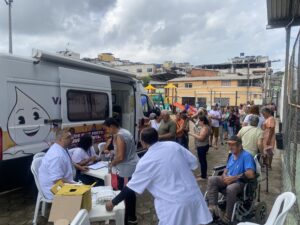 À esquerda, veículo de vacinação móvel estacionado. À frente, profissionais de saúde com os imunizantes, seguidos de uma fila expressiva de idosos para se vacinar.
